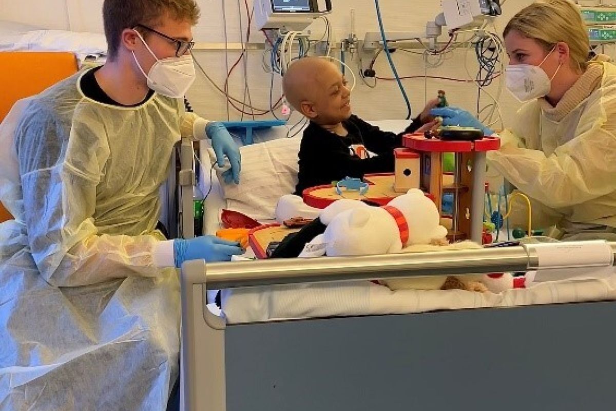 zwei erwachsene in steriler kleidung am krankenbett eines krebskranken kindes